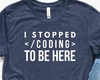 May include: A dark blue short-sleeved t-shirt with white text that reads I STOPPED </CODING> TO BE HERE, paired with light blue distressed denim jeans and a pair of white low-top canvas sneakers with red and blue trim on the rubber soles.