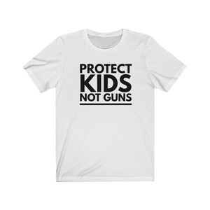 May include: White t-shirt with black text that reads "PROTECT KIDS NOT GUNS".
