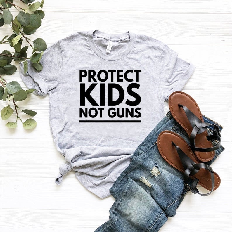 May include: A gray t-shirt with the text "PROTECT KIDS NOT GUNS" printed in black.
