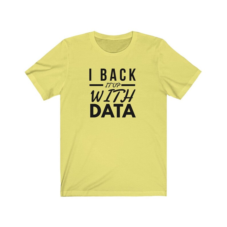 Puede incluir: Una camiseta de manga corta de color amarillo claro con texto negro centrado en el pecho que dice I BACK IT UP WITH DATA, con las palabras I BACK y DATA en una fuente sans-serif negrita y las palabras IT UP en una fuente m&aacute;s fina.
