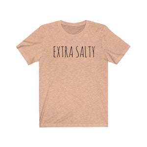 May include: A light peach colored t-shirt with the text "EXTRA SALTY" printed in black.