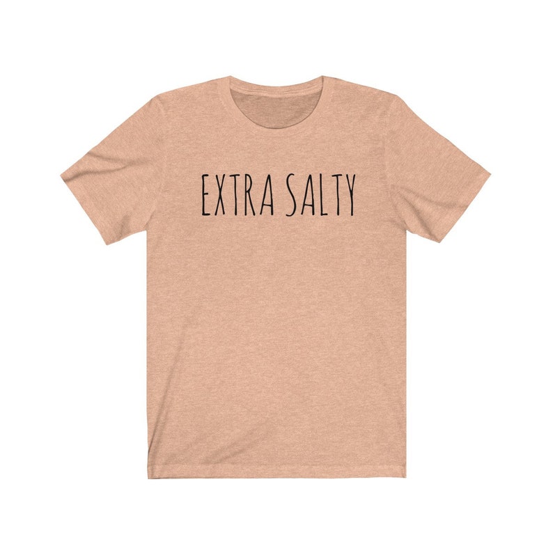 May include: A light peach colored t-shirt with the text "EXTRA SALTY" printed in black.