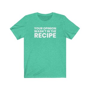 May include: A heathered mint green short-sleeved t-shirt featuring the white text "YOUR OPINION WASN'T IN THE RECIPE" printed in a bold, sans-serif font across the centre of the chest. The garment has a crew neckline and a standard fit.