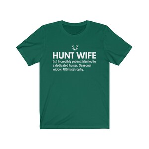 May include: A green t-shirt with white text that reads "HUNT WIFE (n.) Incredibly patient; Married to a dedicated hunter; Seasonal widow; Ultimate trophy."