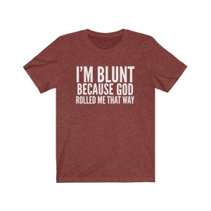 May include: Maroon t-shirt with the text "I'M BLUNT BECAUSE GOD ROLLED ME THAT WAY" in white block letters. The shirt has short sleeves and a crew neck. The fabric has a heathered texture.
