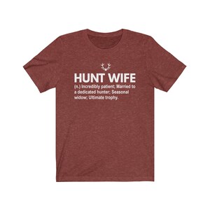 May include: Red t-shirt with white text that reads "HUNT WIFE (n.) Incredibly patient; Married to a dedicated hunter; Seasonal widow; Ultimate trophy."