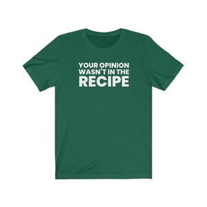 May include: A dark green short-sleeved t-shirt featuring the white text "YOUR OPINION WASN'T IN THE RECIPE" printed in a bold, sans-serif font across the centre of the chest. The garment has a crew neckline and a standard, straight-cut silhouette.
