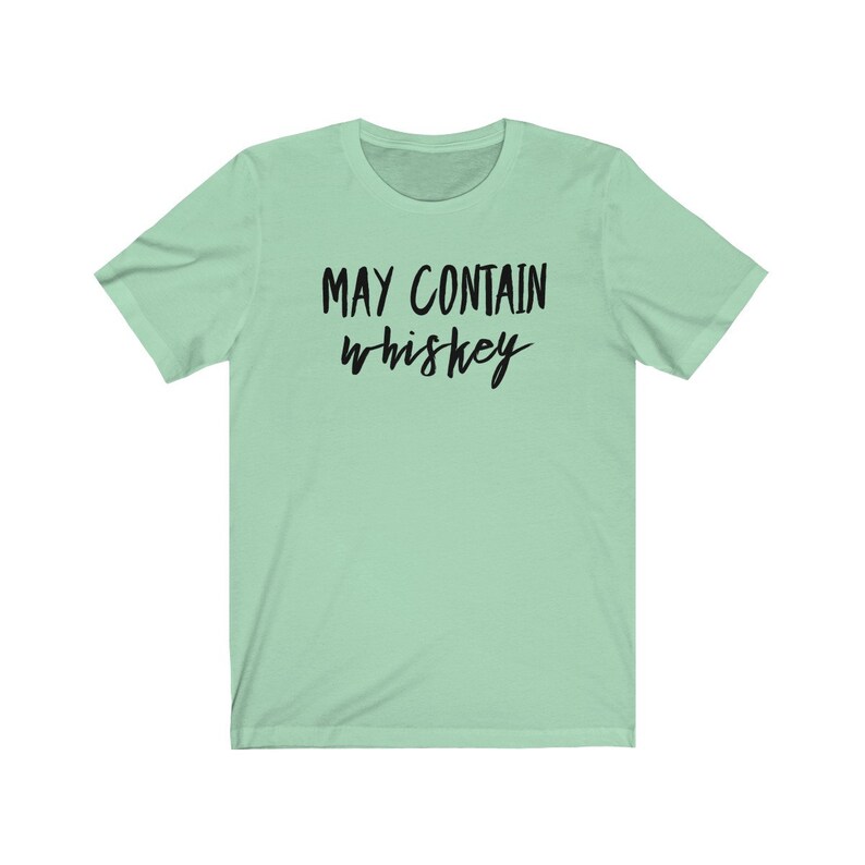 May include: A light green t-shirt with the text "MAY CONTAIN whiskey" in black script. The shirt has short sleeves and a crew neck. The text is centered on the front of the shirt.