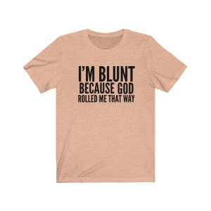 May include: A light brown t-shirt with the text "I'M BLUNT BECAUSE GOD ROLLED ME THAT WAY" printed in black.