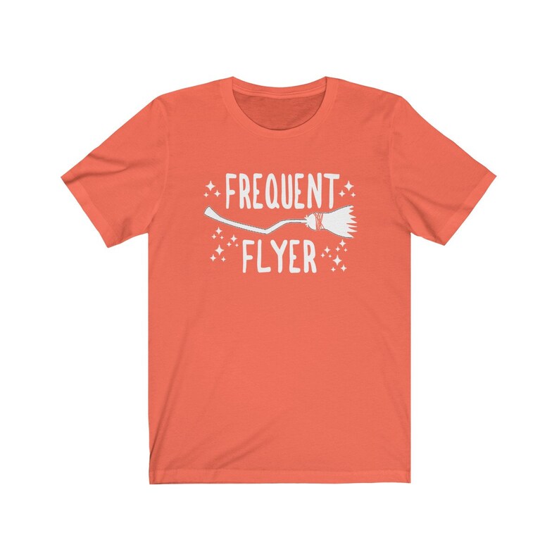 May include: A coral orange t-shirt with a white graphic of a broom and the text "Frequent Flyer".