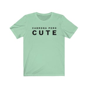 May include: A light green t-shirt with the text "Cabrona Pero Cute" printed in black.