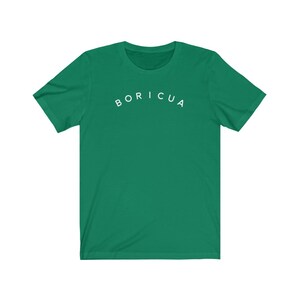 Puede incluir: Una camiseta verde con la palabra "BORICUA" arqueada en letras blancas en el pecho. La camiseta tiene mangas cortas y cuello redondo. La tela parece ser un material suave y ligero.