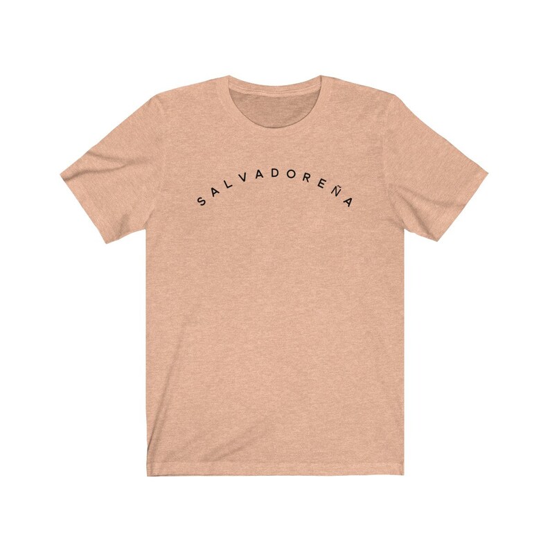 May include: A light peach colored t-shirt with the text "SALVADORENA" printed in black in an arc across the chest.