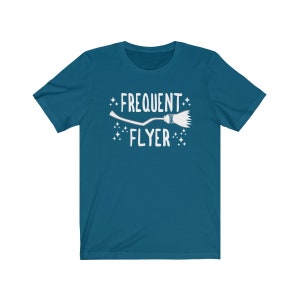 May include: Teal blue t-shirt with a white graphic of a broom and the text "Frequent Flyer".