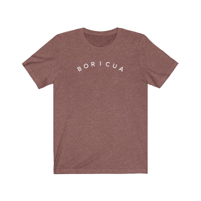 Puede incluir: Una camiseta marr&oacute;n jaspeada de manga corta con la palabra "BORICUA" arqueada en letras blancas en el pecho. La camiseta est&aacute; hecha de un material suave y tiene un cuello redondo cl&aacute;sico.