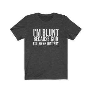 May include: Dark gray t-shirt with the white text "I'M BLUNT BECAUSE GOD ROLLED ME THAT WAY." The shirt has short sleeves and a crew neck. The text is centered on the front of the shirt.
