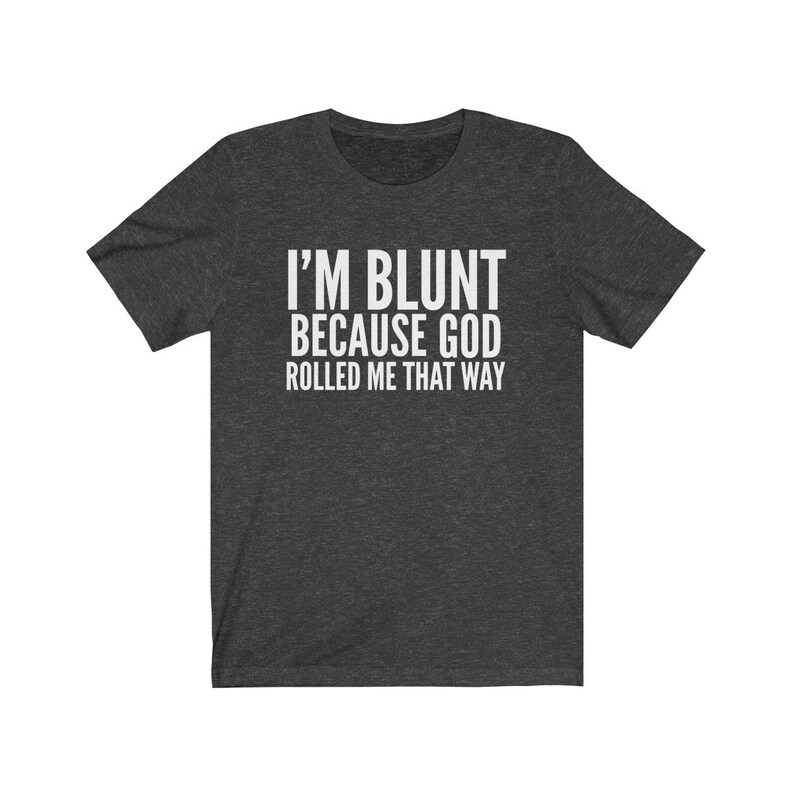 May include: Dark gray t-shirt with the white text "I'M BLUNT BECAUSE GOD ROLLED ME THAT WAY." The shirt has short sleeves and a crew neck. The text is centered on the front of the shirt.
