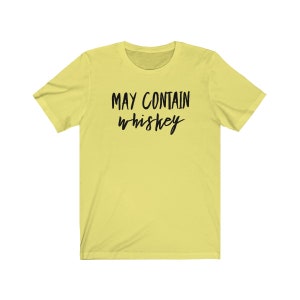 May include: A light yellow t-shirt with the text "MAY CONTAIN whiskey" in black, handwritten-style font. The shirt has short sleeves and a crew neck.