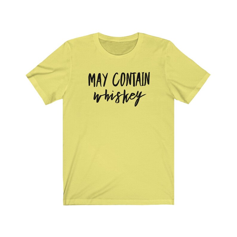 May include: A light yellow t-shirt with the text "MAY CONTAIN whiskey" in black, handwritten-style font. The shirt has short sleeves and a crew neck.