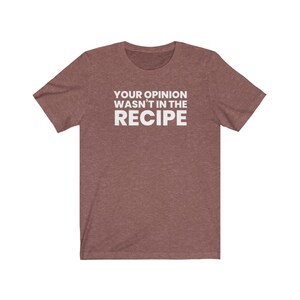 May include: A heathered maroon short-sleeved t-shirt featuring the white text "YOUR OPINION WASN'T IN THE RECIPE" printed in a bold, sans-serif font across the centre of the chest. The garment has a crew neckline and a standard fit.