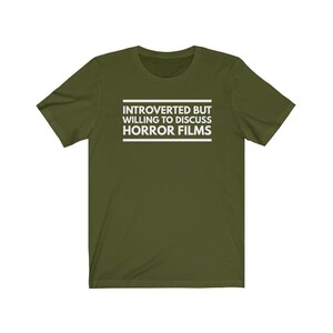 Może przedstawiać: Oliwkowozielony t-shirt z kr&oacute;tkim rękawem z białym napisem wyśrodkowanym na klatce piersiowej o treści: INTROVERTED BUT WILLING TO DISCUSS HORROR FILMS. Tekst jest umieszczony pomiędzy dwiema poziomymi białymi liniami, jedną nad i jedną pod słowami.