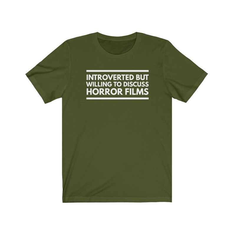 Może przedstawiać: Oliwkowozielony t-shirt z kr&oacute;tkim rękawem z białym napisem wyśrodkowanym na klatce piersiowej o treści: INTROVERTED BUT WILLING TO DISCUSS HORROR FILMS. Tekst jest umieszczony pomiędzy dwiema poziomymi białymi liniami, jedną nad i jedną pod słowami.