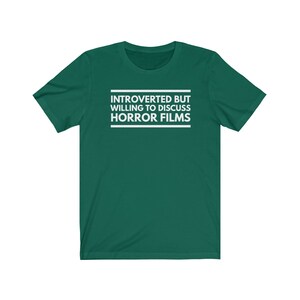 Może przedstawiać: Ciemnozielony t-shirt z kr&oacute;tkim rękawem z białym napisem wyśrodkowanym na klatce piersiowej: INTROVERTED BUT WILLING TO DISCUSS HORROR FILMS. Tekst jest umieszczony pomiędzy dwiema poziomymi białymi liniami, jedną nad i jedną pod napisem.