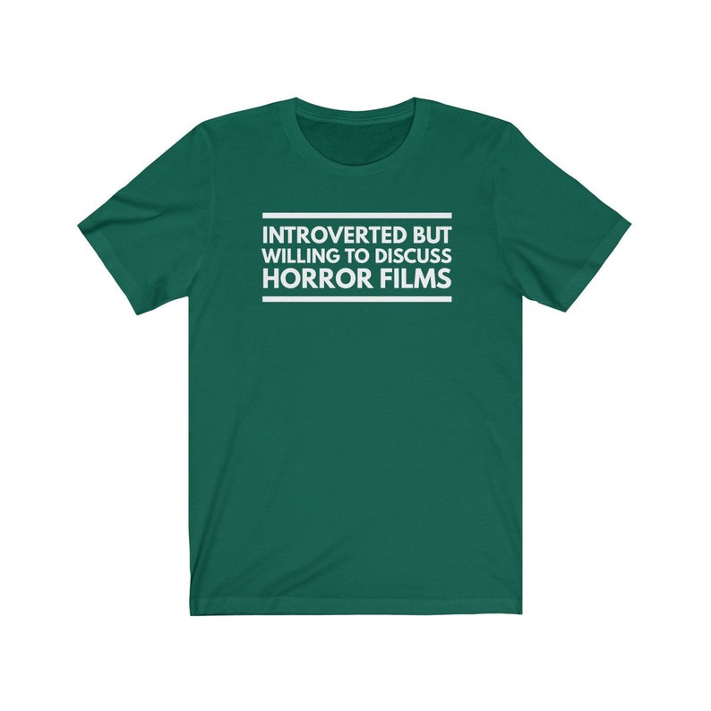 Może przedstawiać: Ciemnozielony t-shirt z kr&oacute;tkim rękawem z białym napisem wyśrodkowanym na klatce piersiowej: INTROVERTED BUT WILLING TO DISCUSS HORROR FILMS. Tekst jest umieszczony pomiędzy dwiema poziomymi białymi liniami, jedną nad i jedną pod napisem.