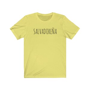 以下が含まれることがあります： 前面に黒い文字で「SALVADORE&Ntilde;A」とプリントされた黄色の半袖Tシャツです。