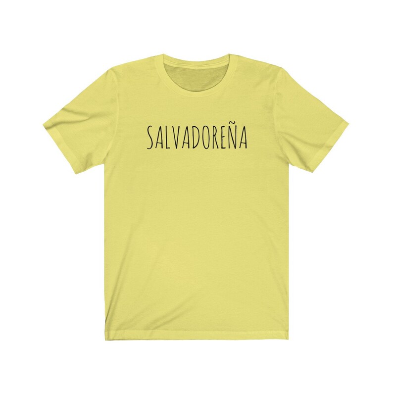 以下が含まれることがあります： 前面に黒い文字で「SALVADORE&Ntilde;A」とプリントされた黄色の半袖Tシャツです。