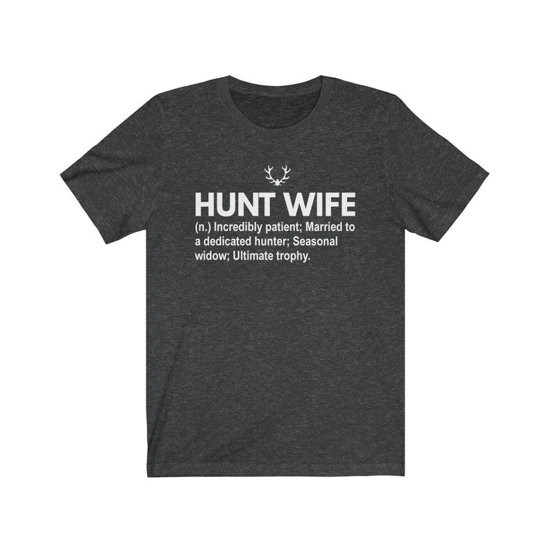 May include: Dark heather grey t-shirt with a white graphic that reads "HUNT WIFE (n.) Incredibly patient; Married to a dedicated hunter; Seasonal widow; Ultimate trophy."