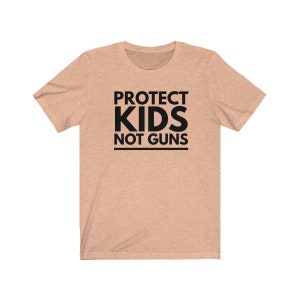 May include: A light peach colored t-shirt with the text "PROTECT KIDS NOT GUNS" printed in black.