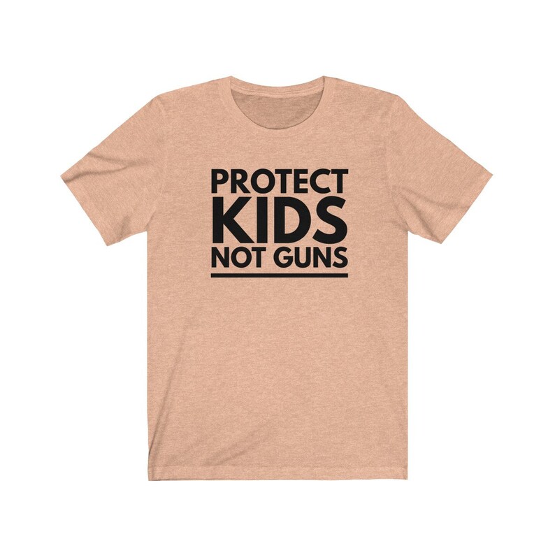 May include: A light peach colored t-shirt with the text "PROTECT KIDS NOT GUNS" printed in black.