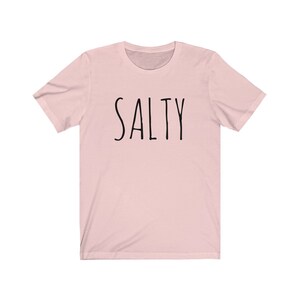 May include: A pink t-shirt with the word "SALTY" printed in black on the front.