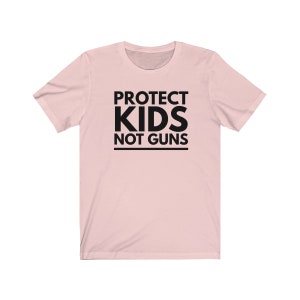 May include: Pink t-shirt with black text that reads "PROTECT KIDS NOT GUNS".