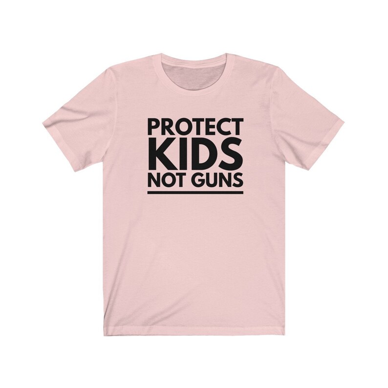 May include: Pink t-shirt with black text that reads "PROTECT KIDS NOT GUNS".