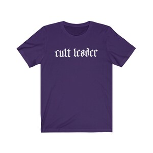 May include: A purple short-sleeved t-shirt with the text "cult leader" in white gothic lettering.