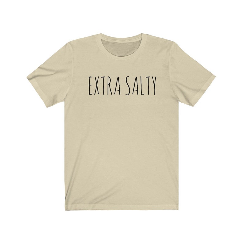May include: A beige short-sleeved t-shirt with the text "EXTRA SALTY" printed in black on the front.