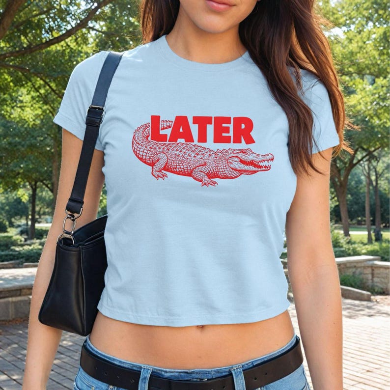 May include: A light blue cropped t-shirt with a red alligator graphic and the word "LATER" printed in red.
