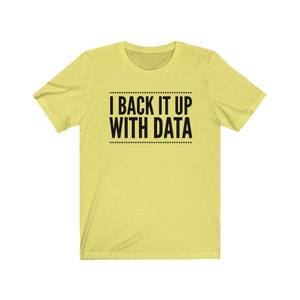May include: A light yellow short-sleeved t-shirt featuring the black text I BACK IT UP WITH DATA centered on the chest. The text is enclosed between two horizontal lines made of small dots, creating a clean and simple graphic design.