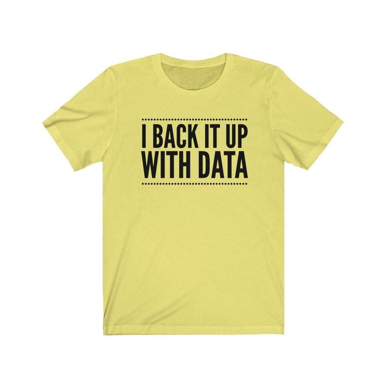 May include: A light yellow short-sleeved t-shirt featuring the black text I BACK IT UP WITH DATA centered on the chest. The text is enclosed between two horizontal lines made of small dots, creating a clean and simple graphic design.