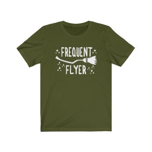 May include: A green t-shirt with a white graphic of a broom and the text "Frequent Flyer" with stars on either side.