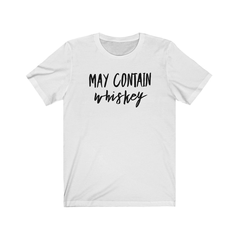 May include: White t-shirt with the phrase "MAY CONTAIN whiskey" printed in black, cursive lettering. The shirt has short sleeves and a crew neck.