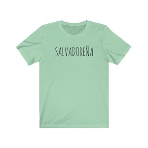 以下が含まれることがあります： 黒で「SALVADORE&Ntilde;A」とプリントされた薄い緑色のTシャツです。