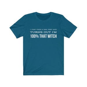 May include: A teal short-sleeve t-shirt featuring white text printed on the chest that reads: I JUST TOOK A DNA TEST AND TURNS OUT I'M 100% THAT WITCH. The shirt has a crew neckline and a standard fit, providing a clear view of the graphic design.