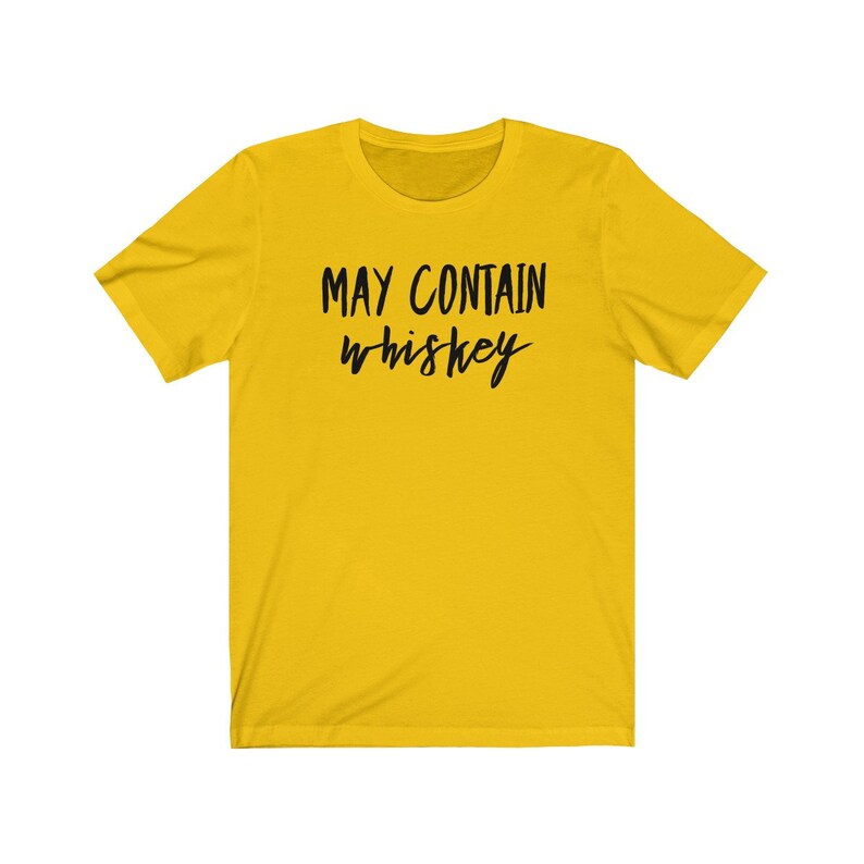 May include: A yellow short-sleeve t-shirt with the text "MAY CONTAIN whiskey" in black script. The shirt has a crew neck and a casual style, suitable for everyday wear.