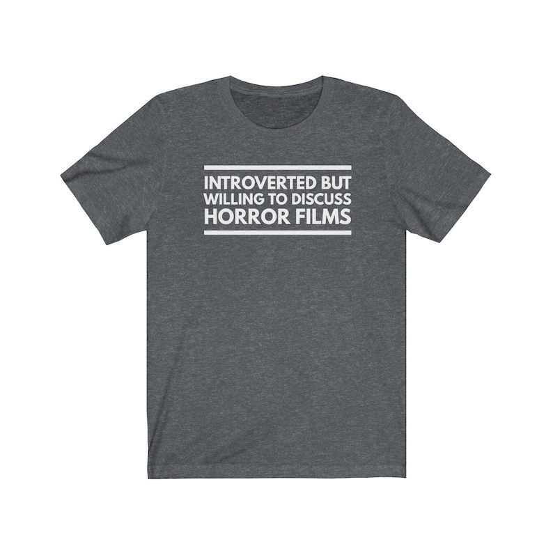 Może przedstawiać: Ciemnoszary melanżowy t-shirt z kr&oacute;tkim rękawem z białym napisem na środku klatki piersiowej: INTROVERTED BUT WILLING TO DISCUSS HORROR FILMS. Tekst jest umieszczony pomiędzy dwiema poziomymi białymi liniami, tworząc przejrzysty projekt graficzny.