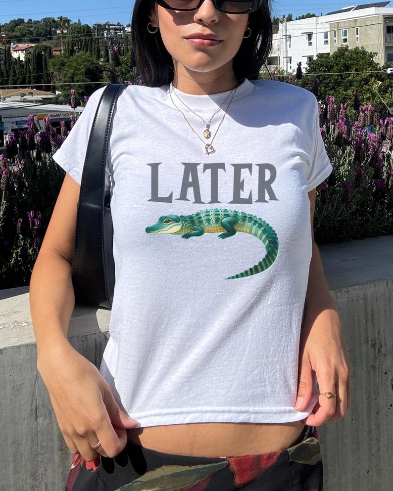 May include: White t-shirt with the word "LATER" printed in gray and a green alligator graphic.