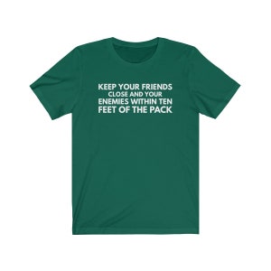 May include: A green t-shirt with the text "KEEP YOUR FRIENDS CLOSE AND YOUR ENEMIES WITHIN TEN FEET OF THE PACK" printed in white.