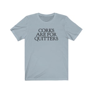 May include: A light blue t-shirt with the text "Corks Are For Quitters" printed in black.